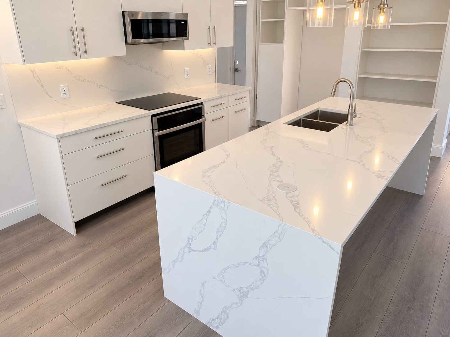 Kitchen island with a veined countertop, sink, and white cabinetry