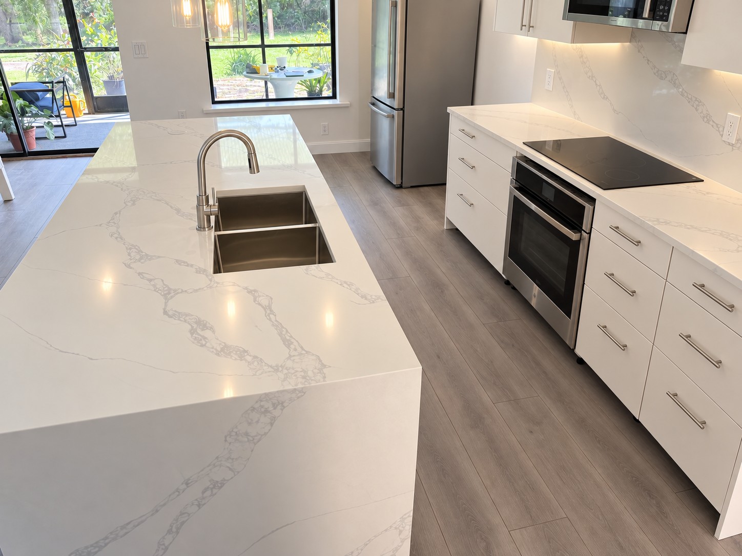 White kitchen viewed from the island, with a double sink, cooktop, and garden-facing windows